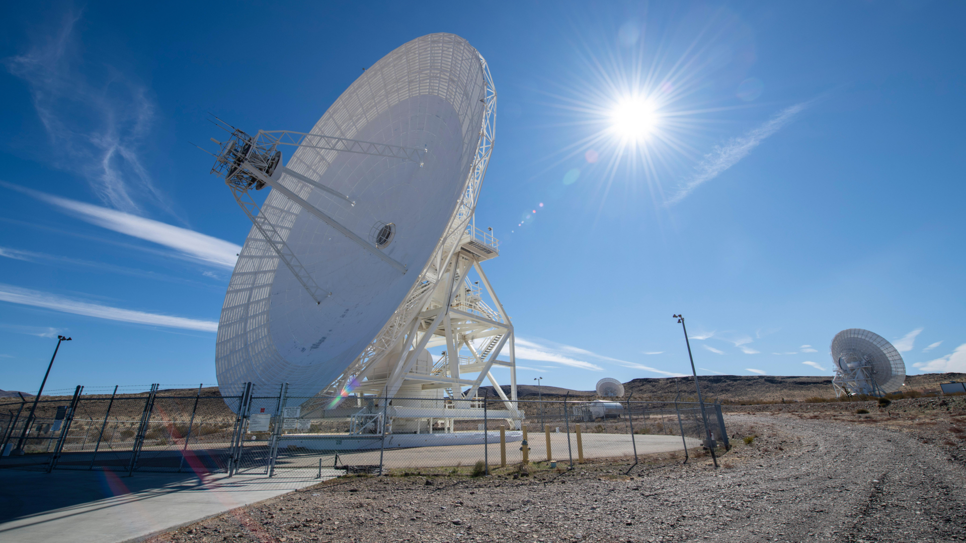 A large white antenna dish points to the left of the screen with the sun in the blue sky behind it