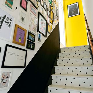 Stairs with a gallery wall above a dark grey half height wall and white stairs painted with black spots