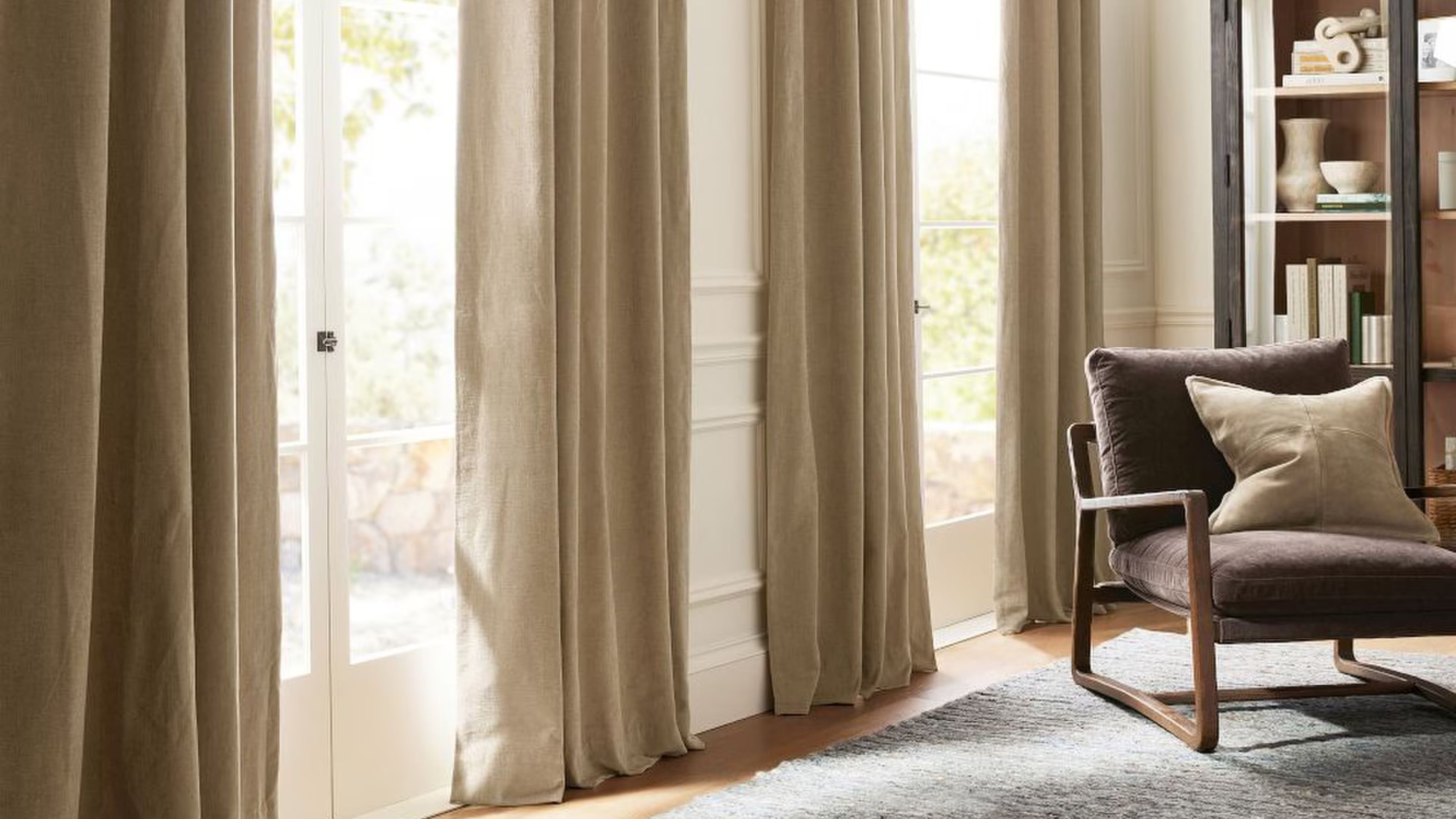 Pottery Barn curtains along a wall of doors with a brown armchair with a cushion, and bookshelf behind