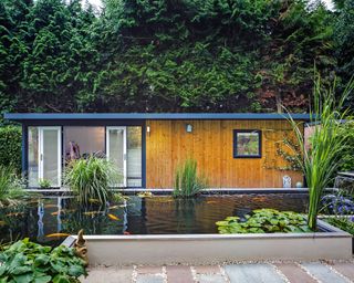 large timber clad garden room with a modern raised pond in front