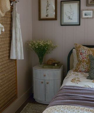 bedroom with floral bedding, a wooden ribbed bedside table and and a gallery wall of floral pictures