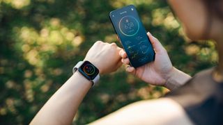 Woman checking a fitness tracker on wrist and app, standing in a sunny park