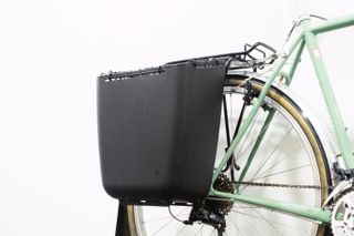 A black plastic tub pannier mounted to a green bike against a white background