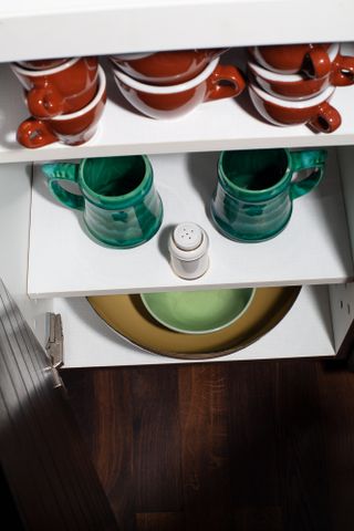 Open cupboard with three shelves containing plates, bowls and cups.