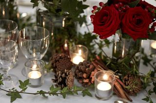 Festive table with vases of red roses and berries, pine cones, cinnamon sticks, foliage garland