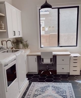 A kitchen with white wall paint decor, black hexagonal floor tile decor, exotic area rug, desk and office chair