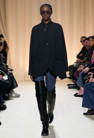 a photo showing some of the best thigh-high boots with a model walking the Bally runway show wearing a navy coat with skinny jeans and black thigh-high boots