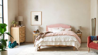 Learning how to zone a bedroom like this can be helpful. There is a pink bed with side tables, an area for dressing, a mirrored space and a red armchair on white rug for relaxing