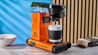 the technivorm moccamaster cup-one, a single serving drip coffee maker that uses number 1 filters and brews exactly 10 oz of coffee in 5 minutes, in bright orange