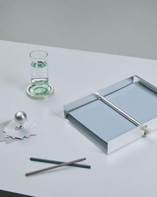 A series of silver objects, including a spherical paper weight, a paper holder, and a glass placer, boast the same retro-inspired shade of silver and minimalist lines.