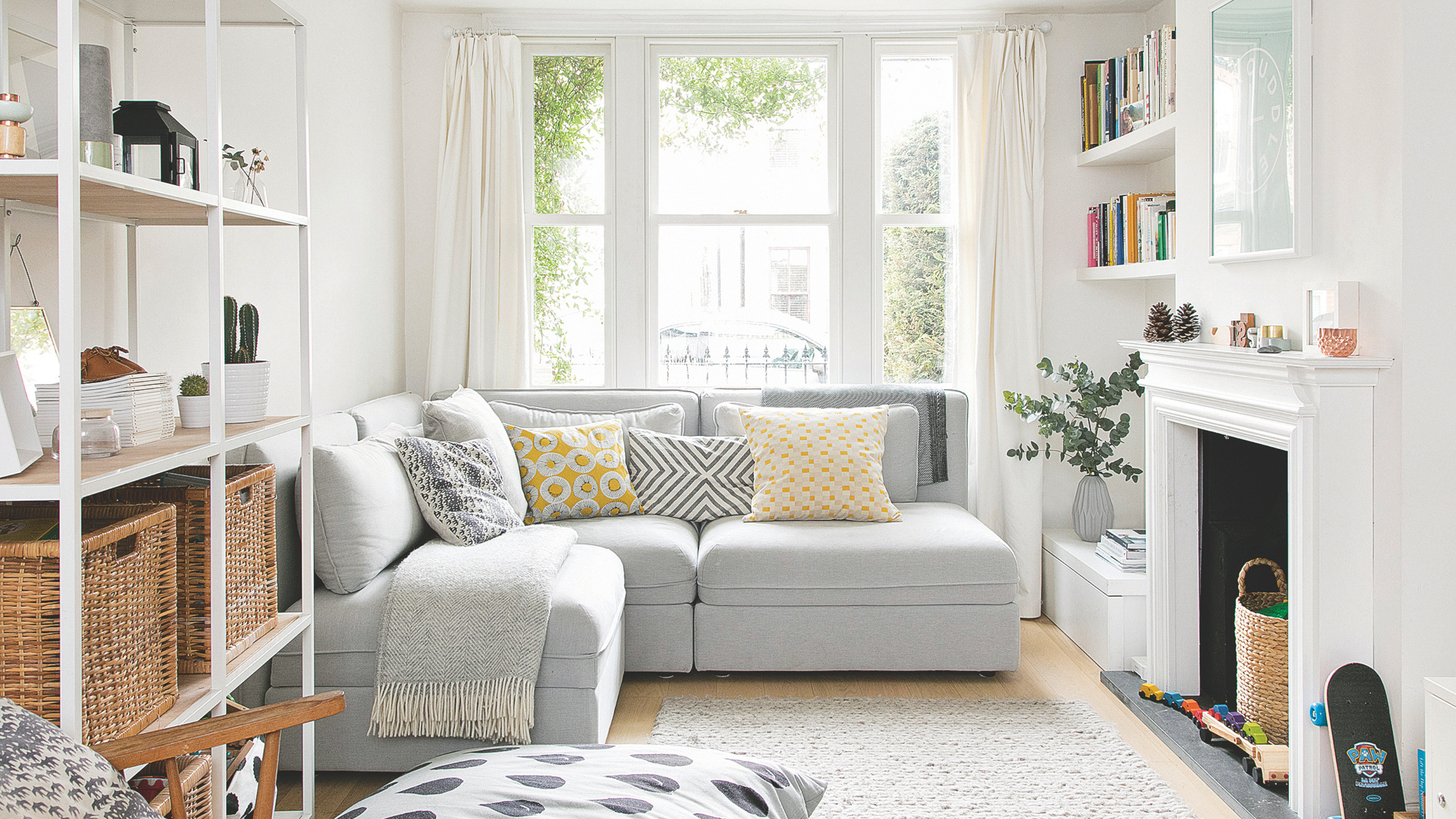 Airy living room with grey sofa, fire place and shelving unit with woven storage boxes.