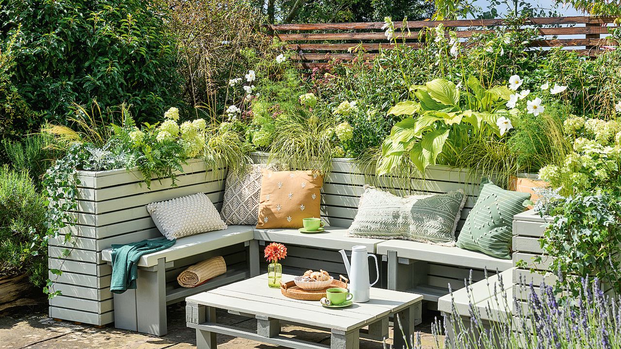 Built-in wooden garden bench with planters and pallet table painted light sage green with filled with overflowing hydrangeas