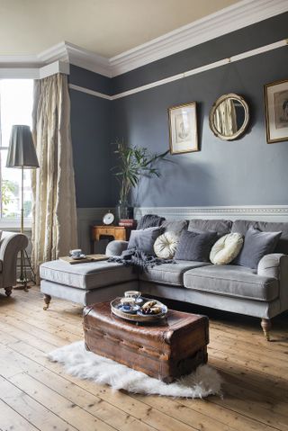 A blue-grey living room paint color idea in an extended Victorian home, with wooden floor and a chest coffee table, and victorian artwork on the walls