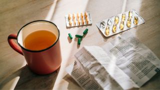 Cup of herbal tea on table next to collection of pills and supplements, highlighting the need to talk about menopause in the South Asian community