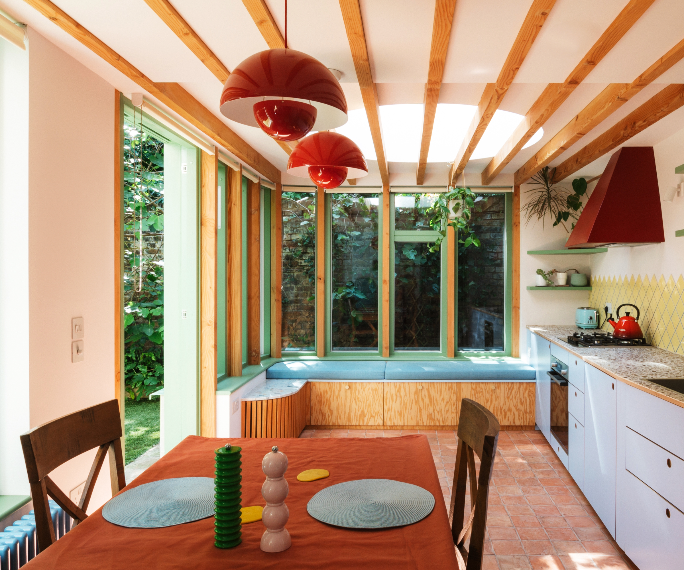 Kitchen extension with wooden beamed ceiling, reading nook along the window and colourful pendant lights