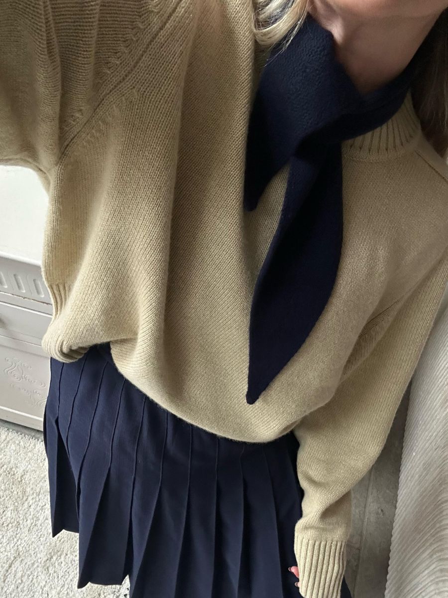 Woman wears beige jumper, navy neck scarf and navy skirt