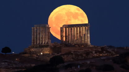 A large golden moon is seen over a series of ancient ruins