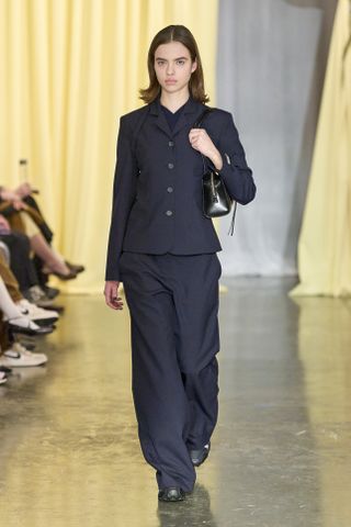 a model walking the runway during Sandy Liang's Fall 2024 show wearing a navy suit and sandy liang x salomon sneakers