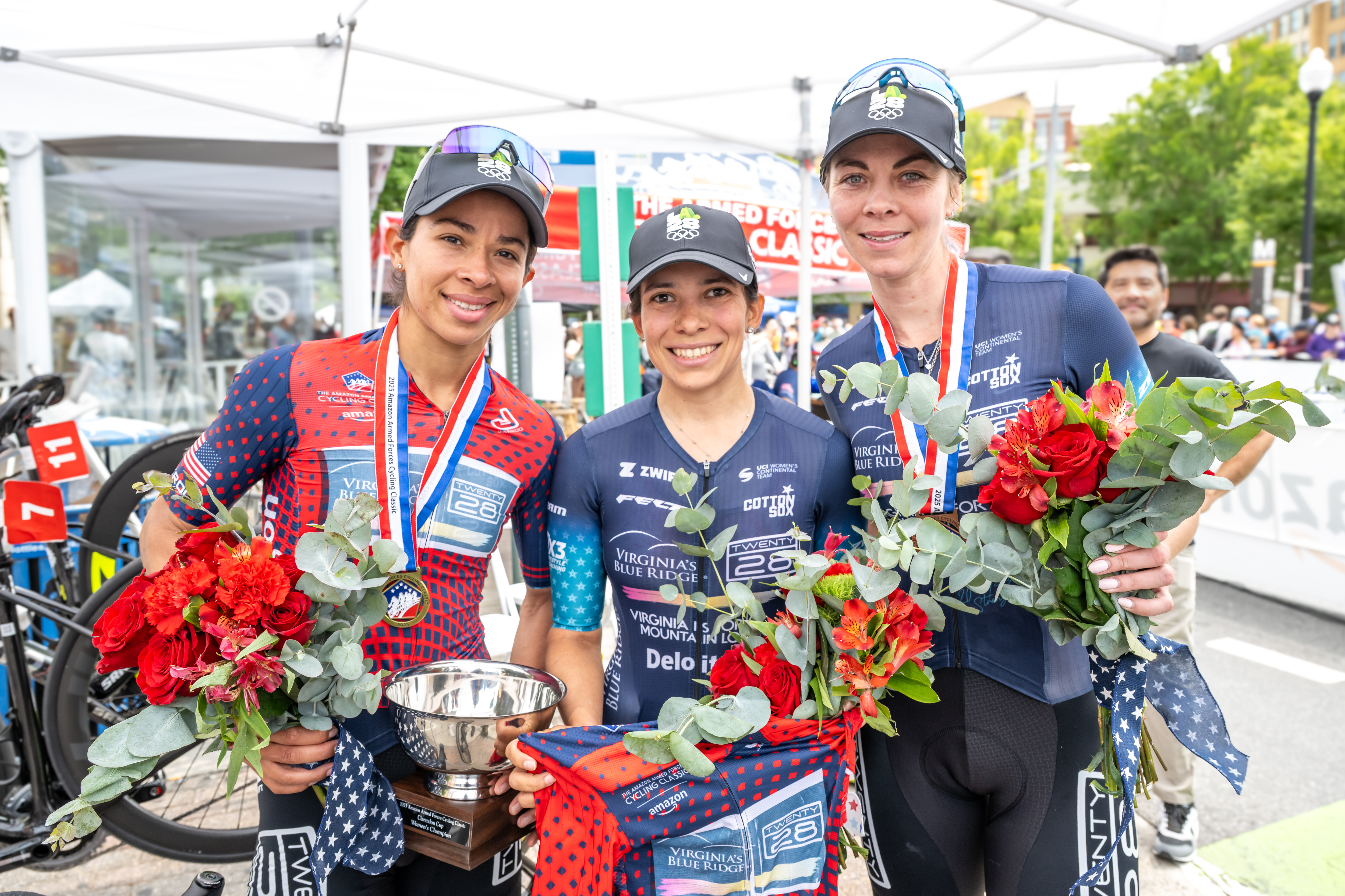 Marlies Mejías celebrates Ominum victory at the 2025 Armed Forces Cycling Classic, wearing the red overall winner's jersey, alongside teammates Sofía Arreola and Emily Erhlich, who also compete on the track