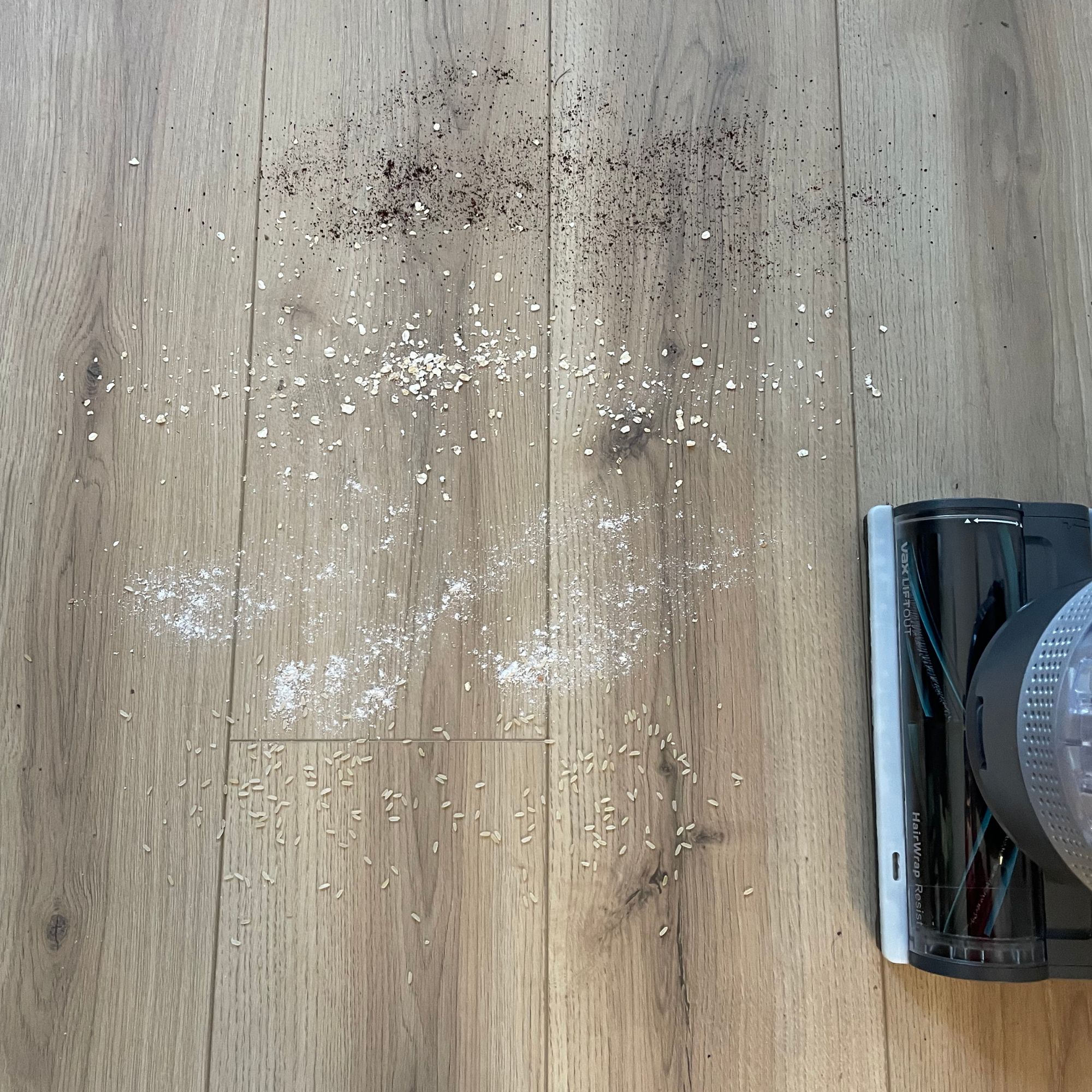 Debris scattered on wood-effect flooring, next to the floorhead of the Vax LiftOut Reach Pet Design Vacuum Cleaner