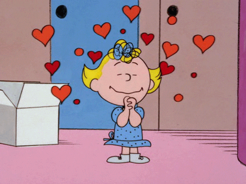 A Peanuts character holds her hands clasped tightly while hearts pulsate around her