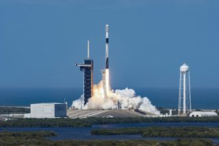 a black-and-white spacex falcon 9 rocket launches into a blue sky.