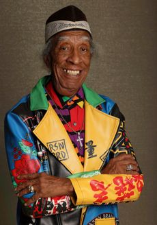 Portrait of Superager William Scott, who leads tours of the city and has the brain power of a fifty-something, even though he is over 80. Scott wears a brigh, multi-colored jacket and shirt.