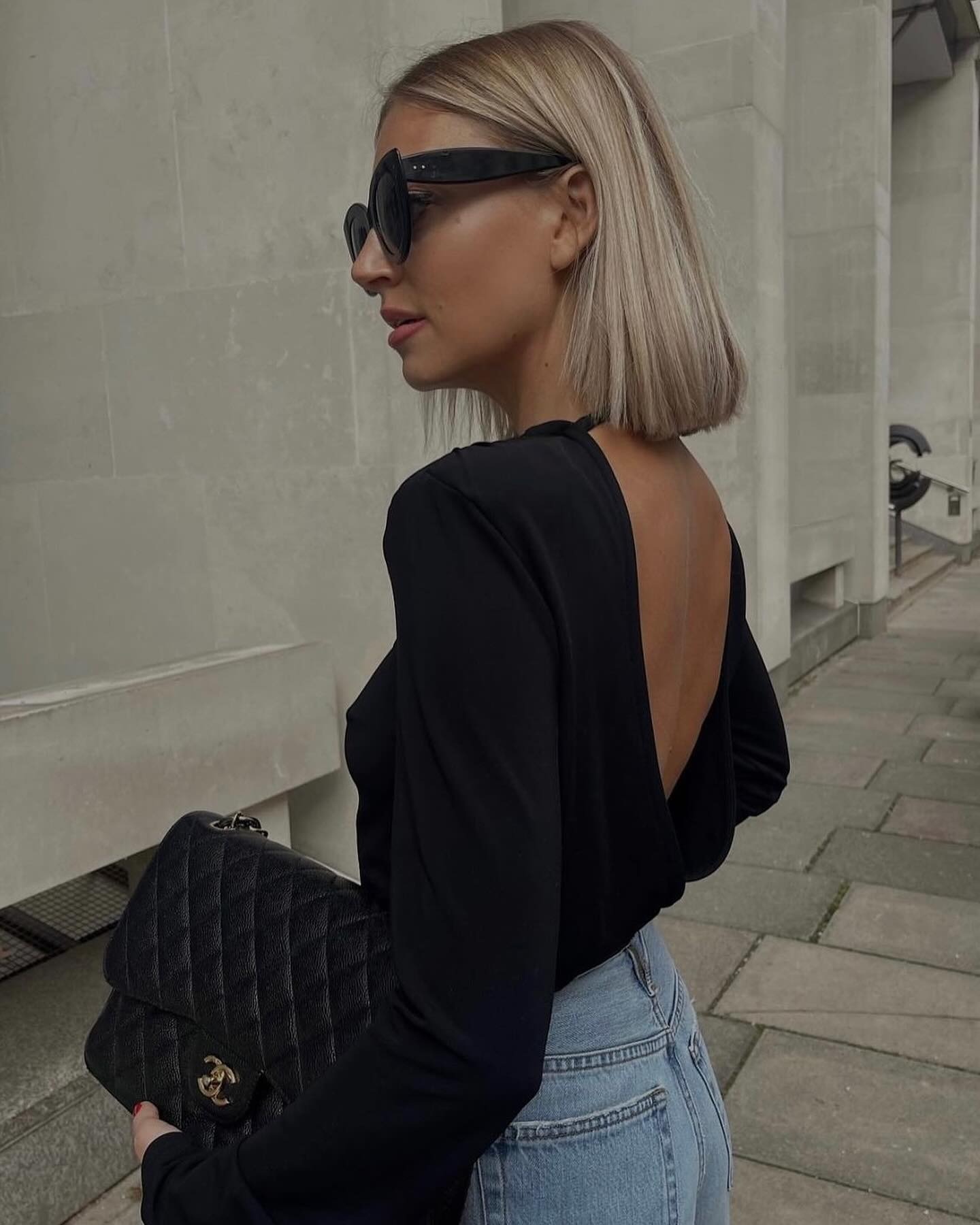A woman wearing a backless top with a blunt, ashy blonde bob