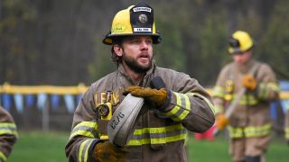 Max Thieriot in fire gear as Bode holding a hose. 