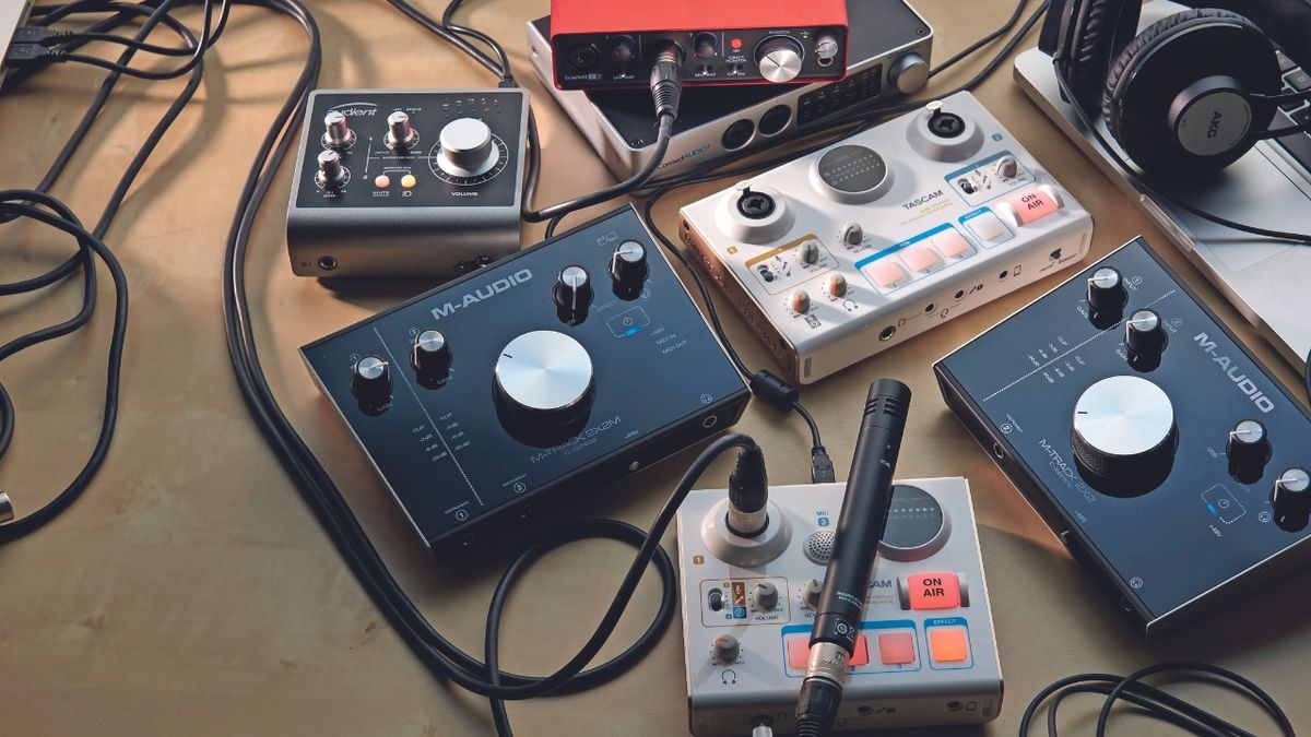 A selection of audio interfaces lying on a desk with instrument cables and microphones