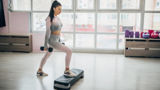 Woman holding light dumbbells stepping up onto a step during walking workout with weights