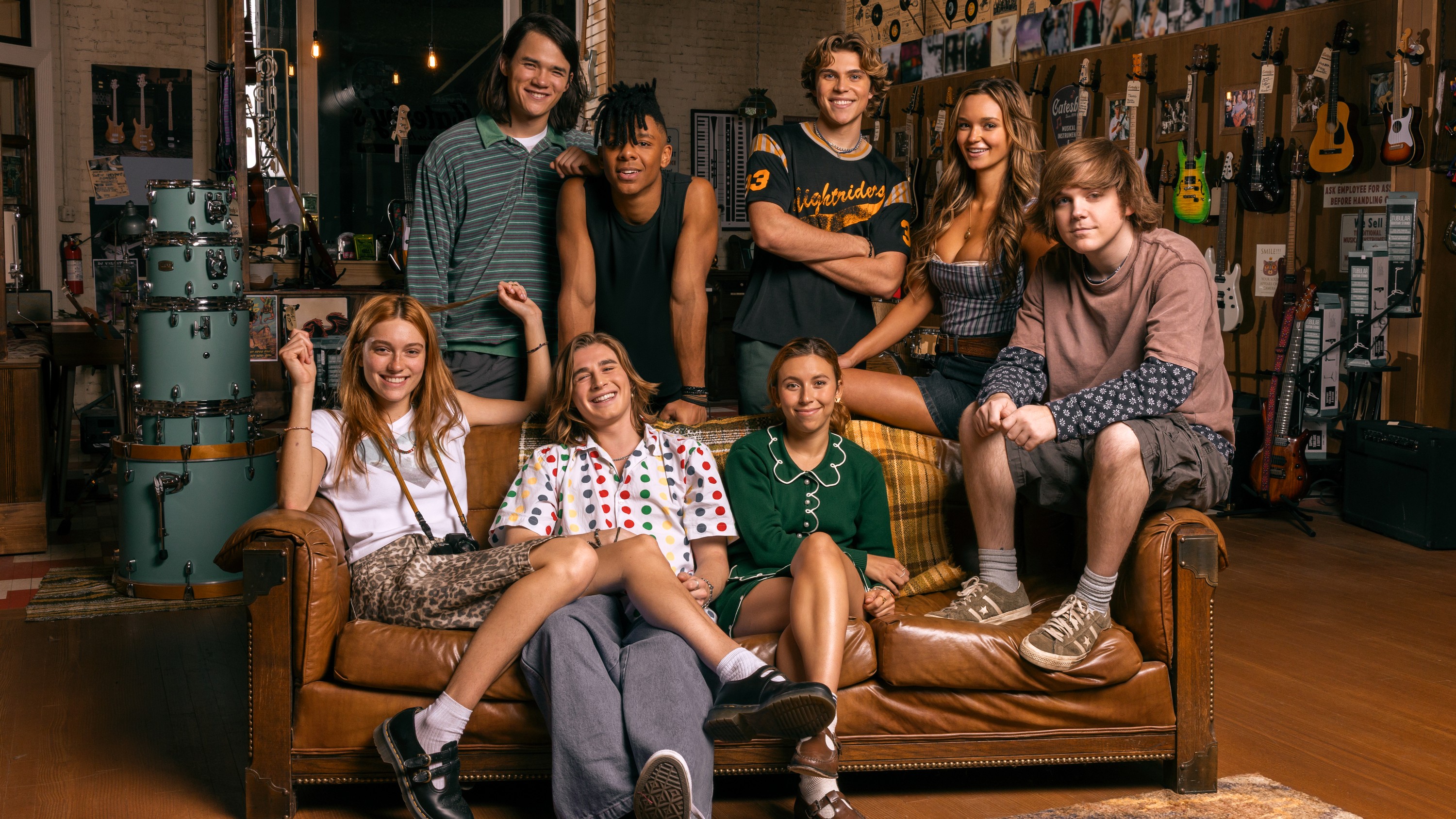 The ensemble cast of Prime Video's "The Runarounds" gathered together around a leather sofa.