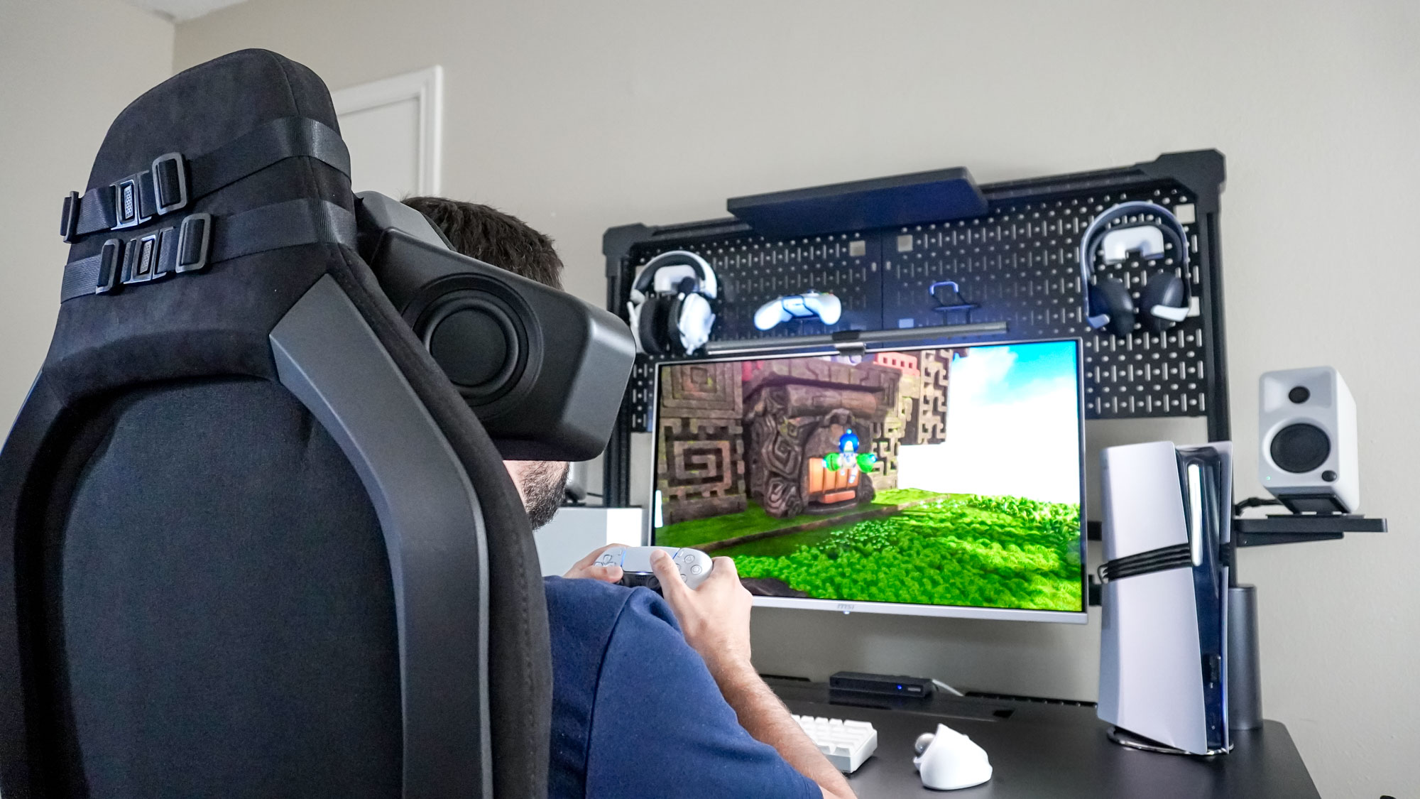 A person sitting in a gaming chair with the Razer Clio head cushion speaker attached to it playing games on PS5 Pro at the Corsair Platform:4 Elevate Desk