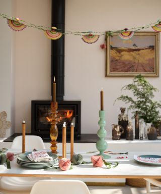 dining table with candles and some decorations, log burner, hanging decoration artwork, plates