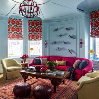 Blue living room with multicoloured curtains and rug, pink sofa and yellow armchairs