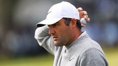 Scottie Scheffler, in a grey jumper, holds his ball behind his head on the 9th hole during the first round