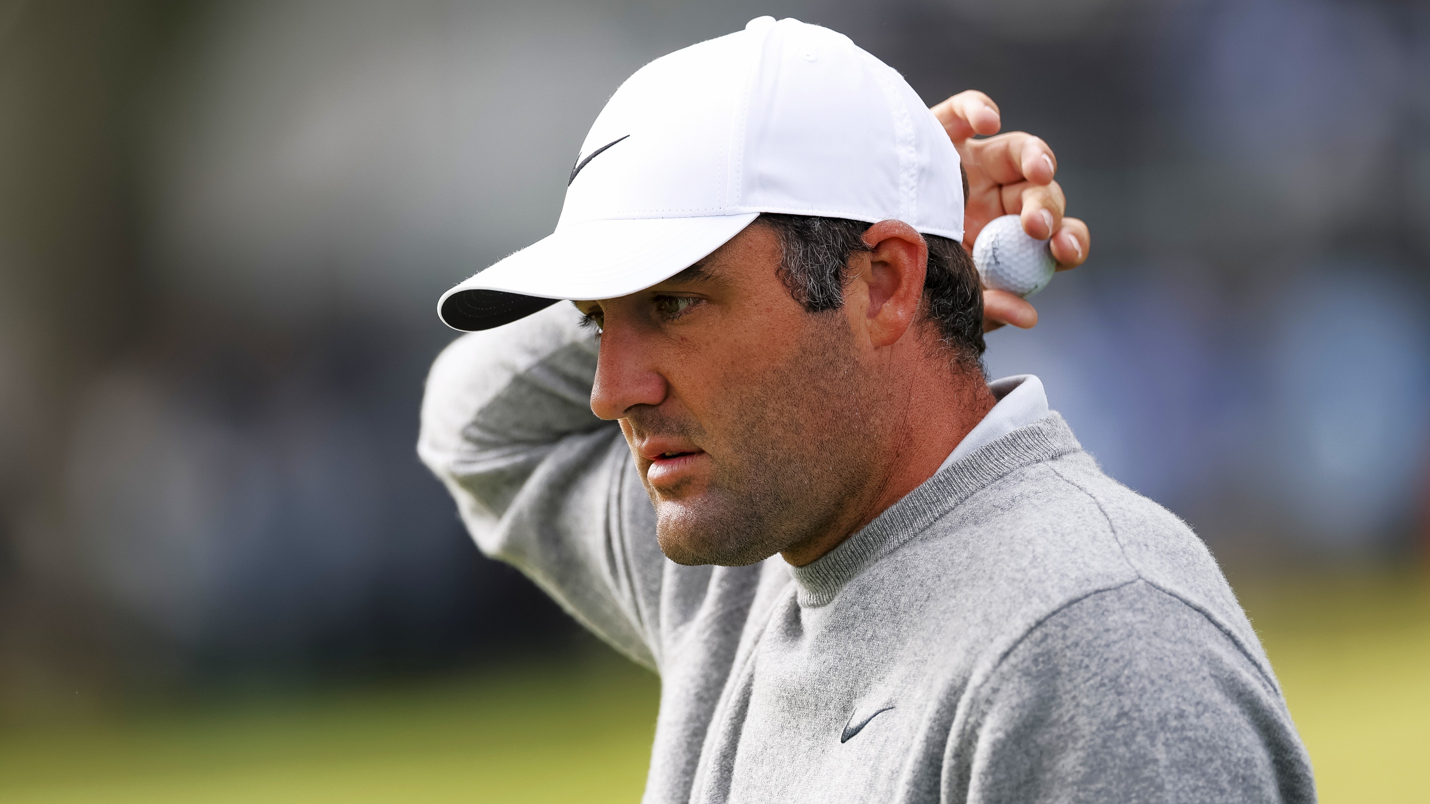 Scottie Scheffler, in a grey jumper, holds his ball behind his head on the 9th hole during the first round