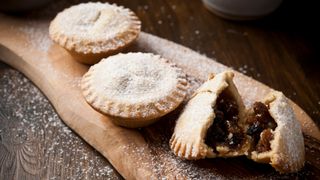 Three mince pies on a wooden board, one broken open