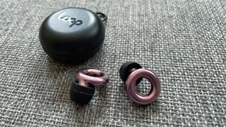 The Loop Experience earplugs in rose gold on a grey surface with their black carry case in the background