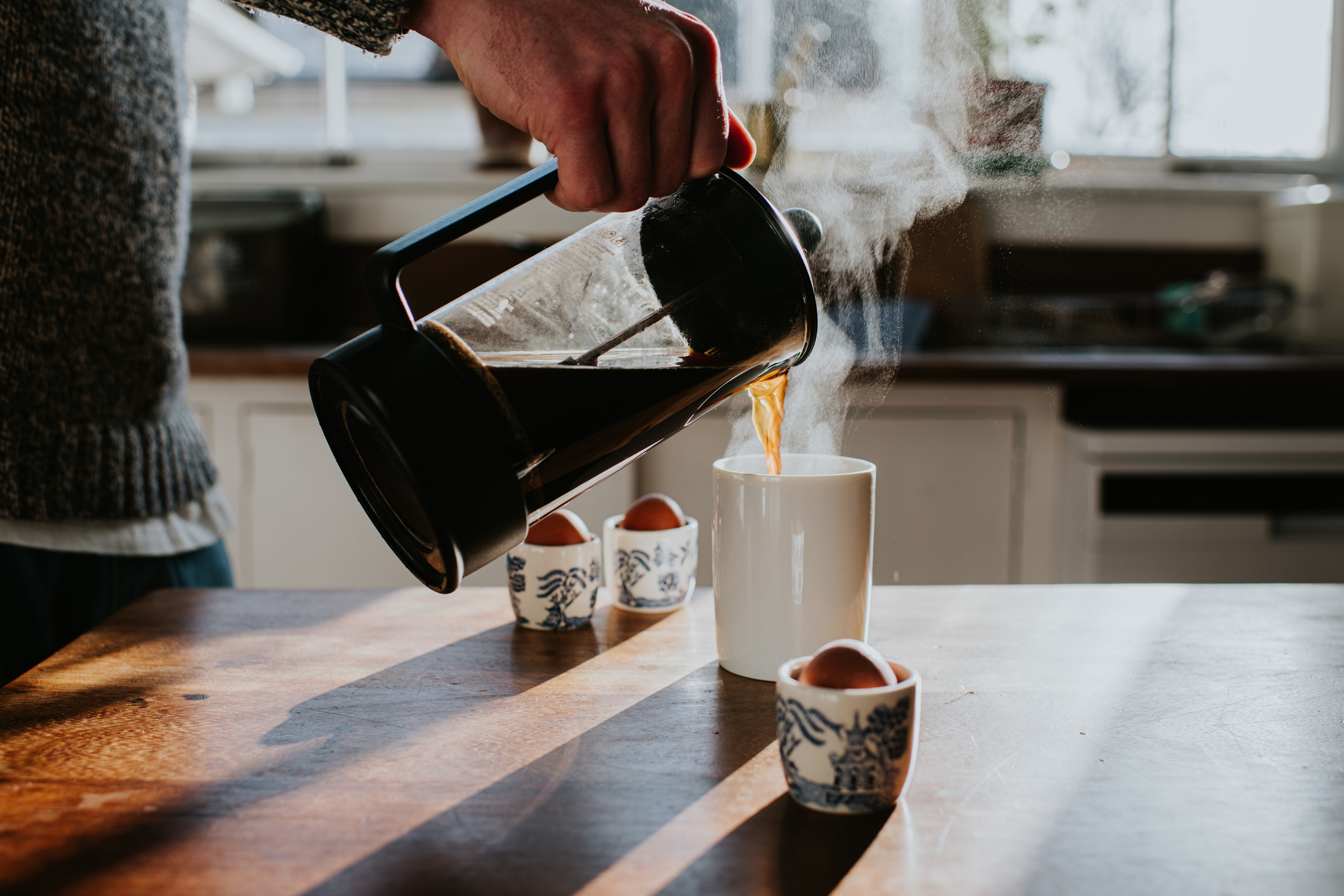 a person pouring fresh coffee from a French press into a mug