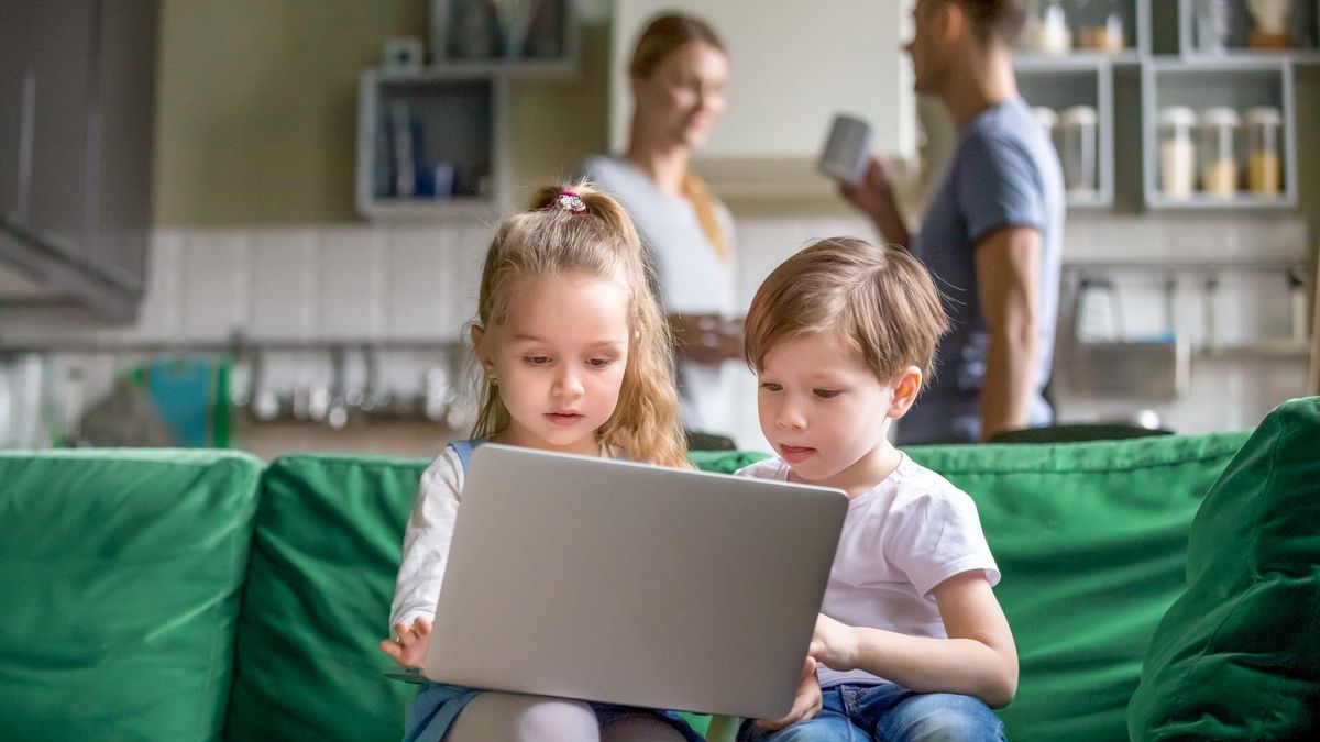 Two children on a laptop with parents in the background