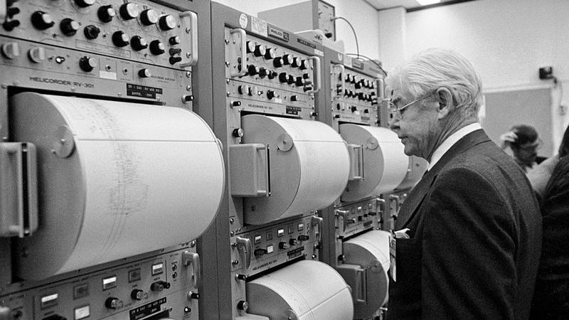 a man in a suit looks at printouts of data rolled into tall machine stacks