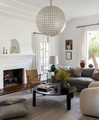 living room with white walls and fire surround and round coffee table with black legs and huge round lampshade and basket work chair