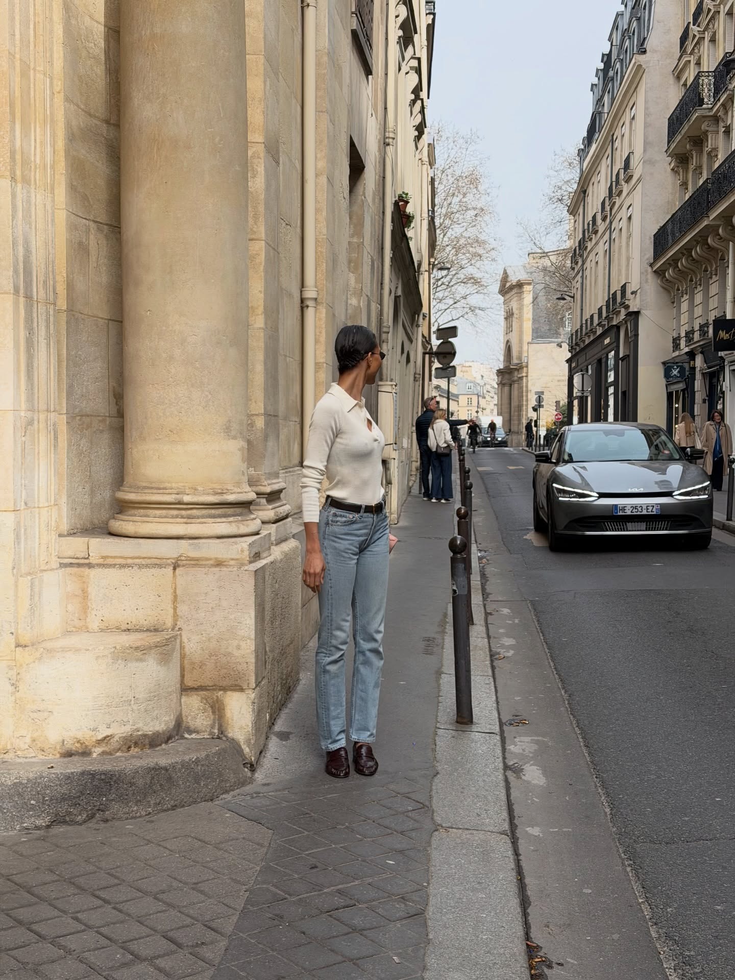 @tylynn wearing a white henley sweater with high-waisted jeans and loafers.