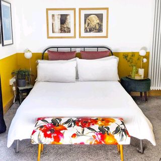 A modern guestroom with yellow paint halfway up the walls, white bedding and wall art