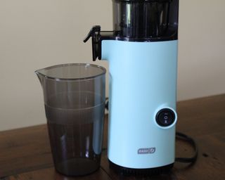 Dash Compact Cold Press Power Juicer and plastic cup on wooden table