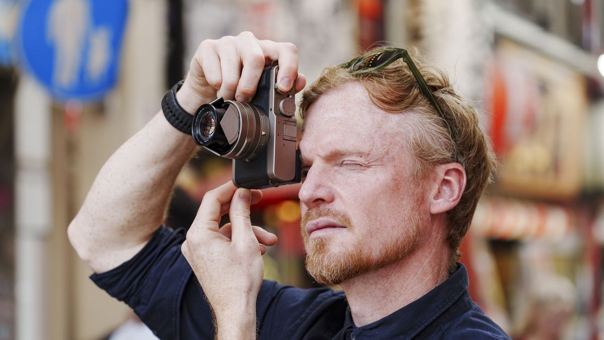 Man holding the Panasonic Lumix L10 compact camera up to his eye, he's looking through the viewfinder, in an urban setting of Japan