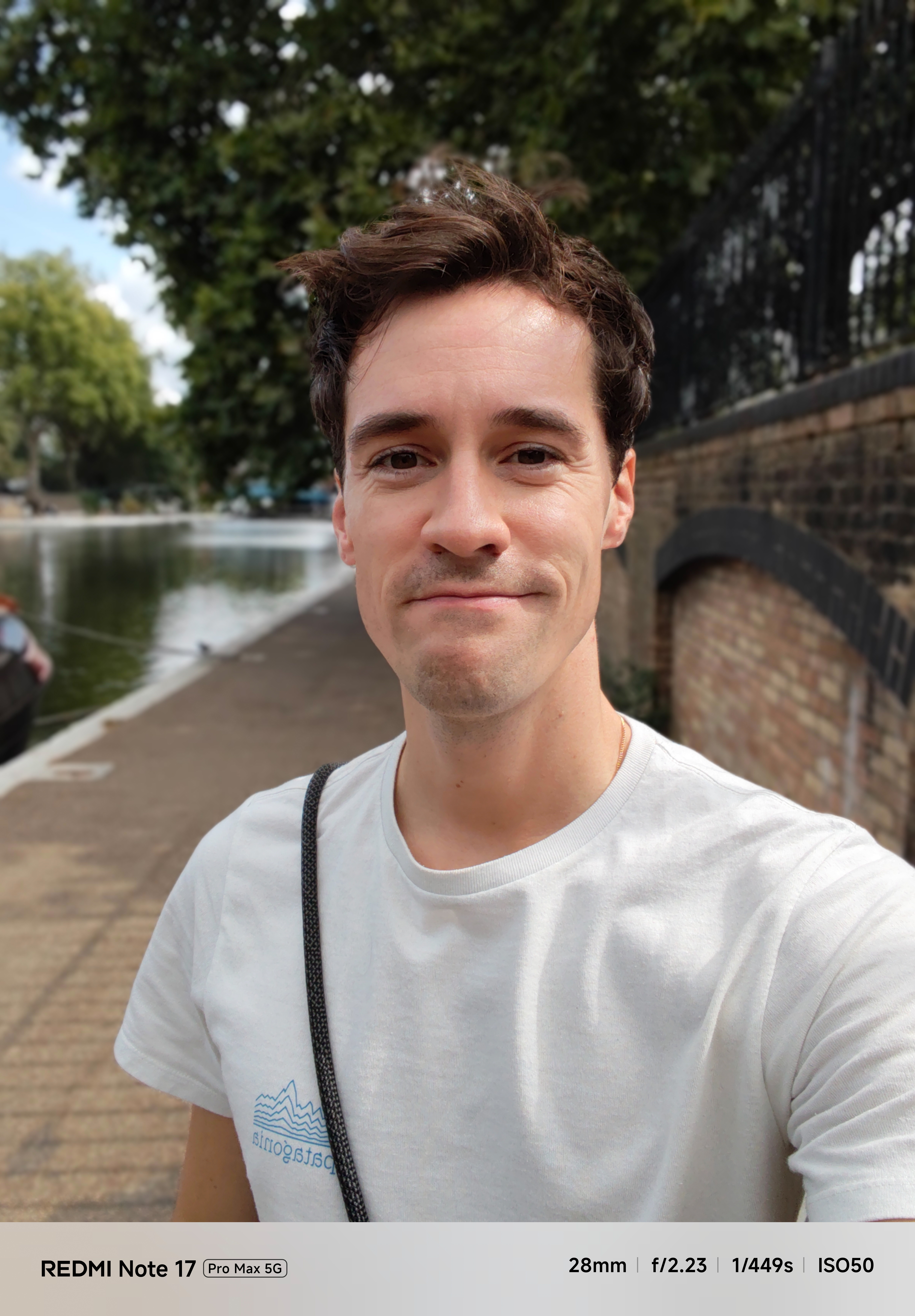 Portrait selfie of a man beside a canal, with the waterside path and trees blurred in the background.