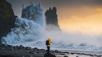 A massive wave hits a cliff on the coast of Iceland at sunset.