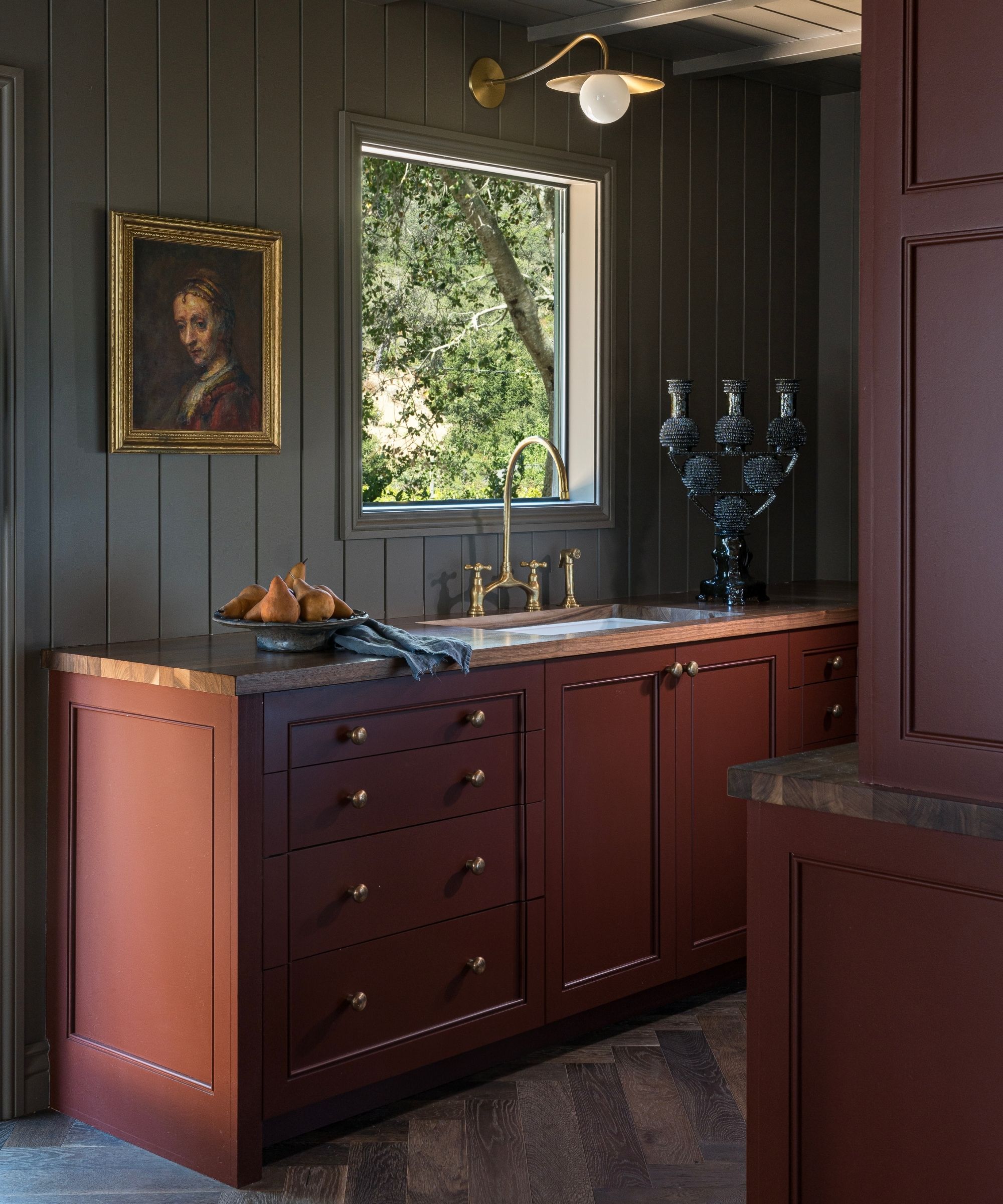 a paneled moody brown kitchen with dark red cabinetry and herringbone dark wooden floor